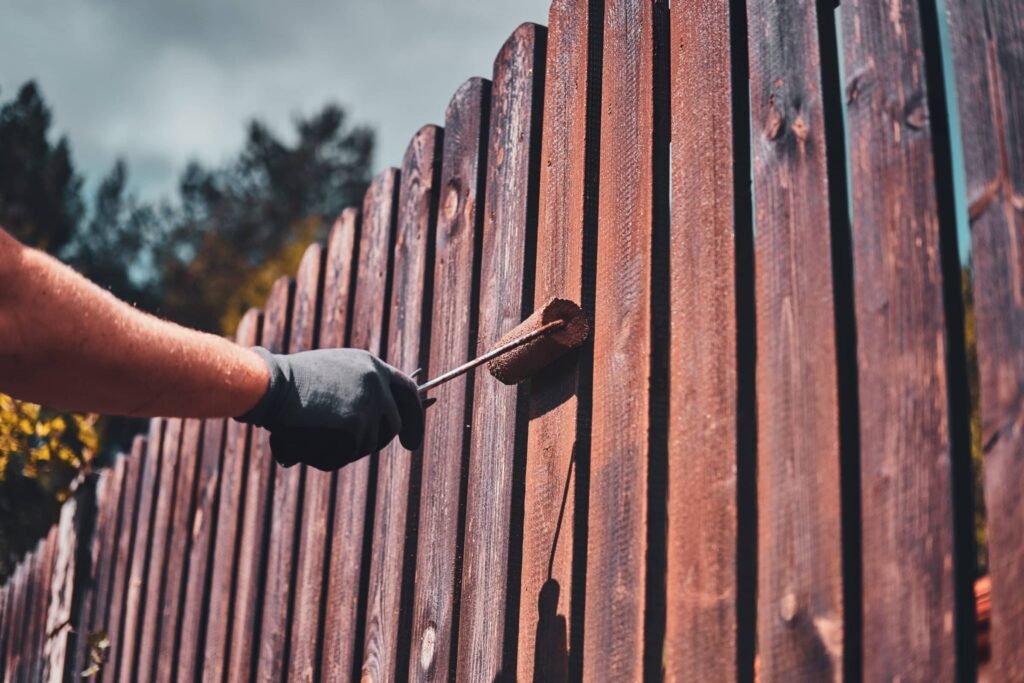 Person painting fence with roller on a cloudy day scaled 1